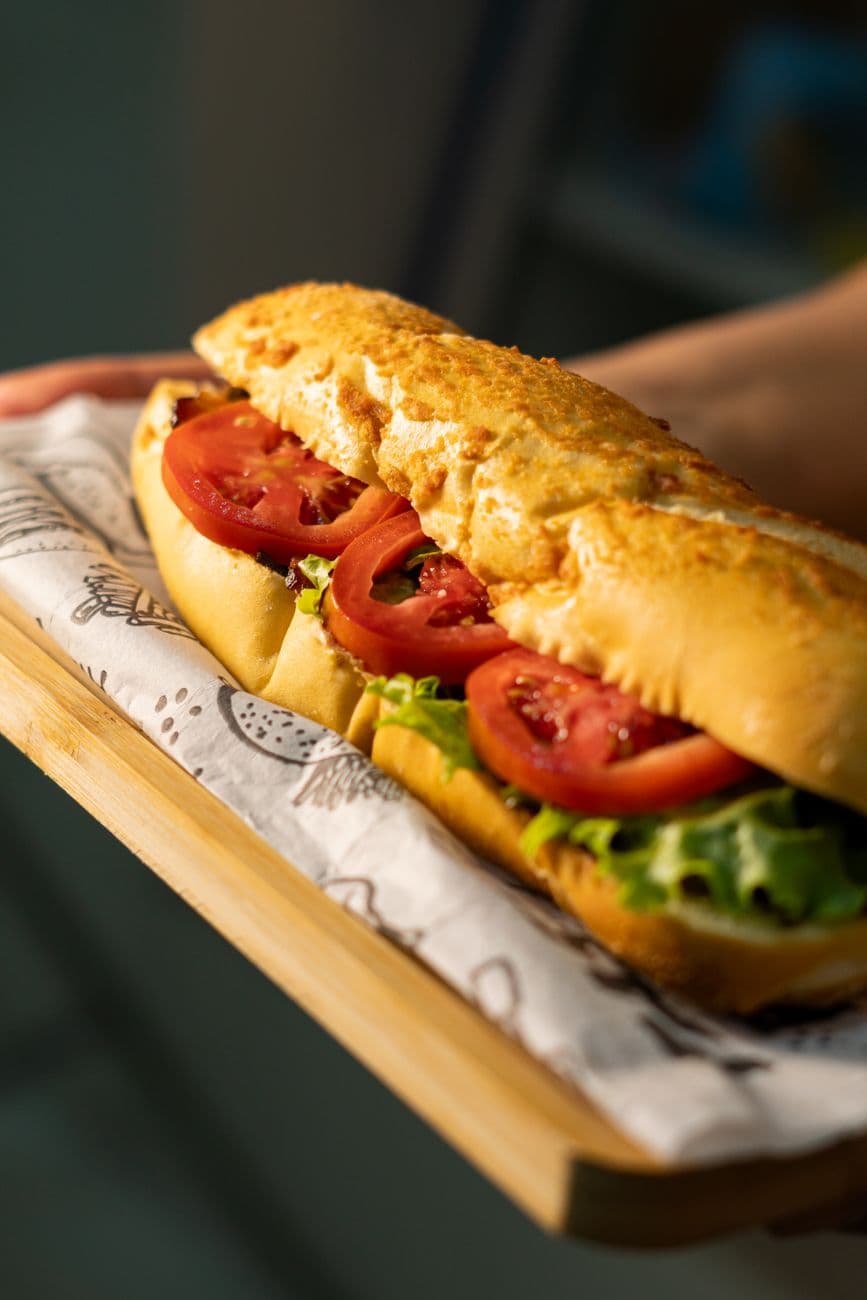 Sandwich sur baguette garni de tomates et de salade fraîche, servi sur une planche en bois