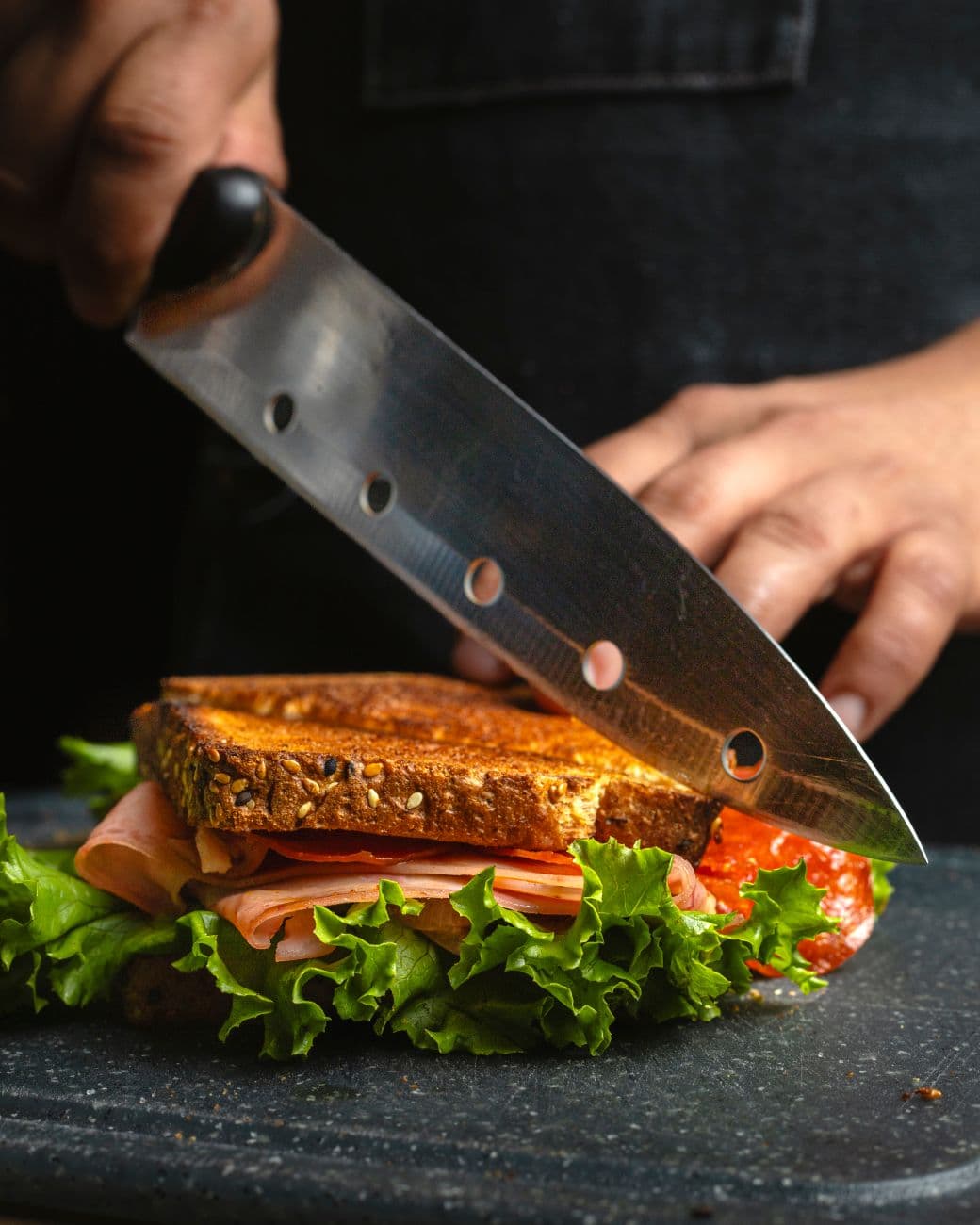 Sandwich jambon, fromage et salade tranché au couteau derrière le comptoir